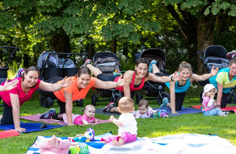 Mamas machen Fitnessübungen im Park, die Kinder spielen