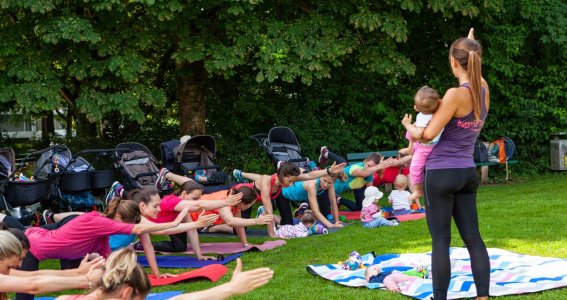 Mamas machen im Park Fitnessübungen mit ihren Babys