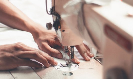 Weißer Stoff wird mit Nähmaschine genäht.