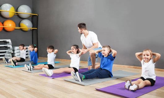 Kinderturnen in Köln Kinder sitzen auf der Matte und machen eine Turnübung