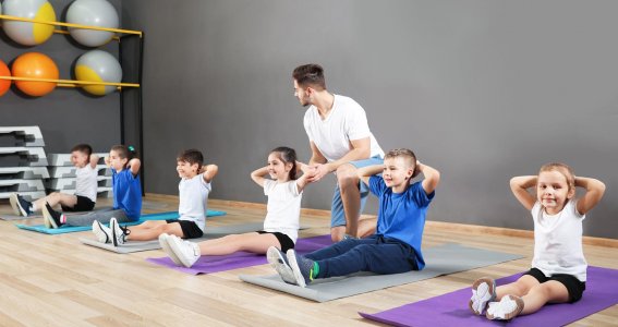 Kinder sitzen auf der Matte und machen eine Turnübung