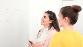 2 Frauen die zu einem Whiteboard blicken und lachen