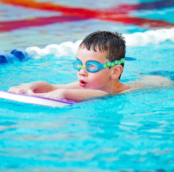 Ein Junge mit Schwimmbrille schwimmt mit einer Schwimmhilfe im Pool