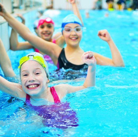 Lachende Mädchen mit Powerpose im Schwimmbecken