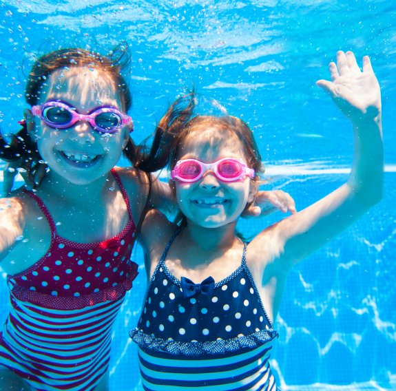 Zwei lachende Kinder unter Wasser sind zu sehen