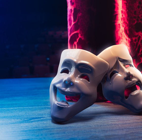 Zwei Schauspielmasken liegen auf einer Bühne