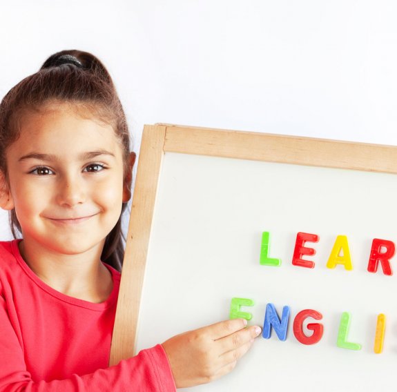 Ein lächelndes Mädchen hält eine weiße Magnettafel mit den bunten Buchstaben "Learn English"