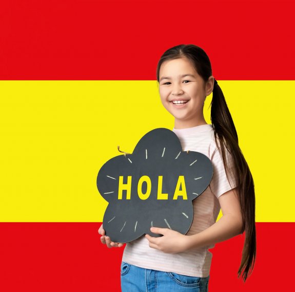 Ein lächelndes Mädchen steht vor dem Hintergrund der spanischen Fahne und hält eine Tafel mit dem Wort "Hola"