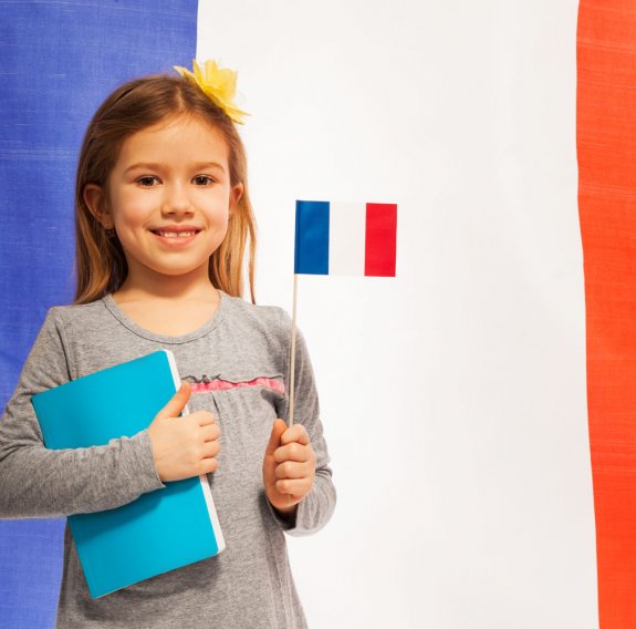 Ein kleines Mädchen hält eine Fahne Frankreichs und ein Heft vor dem Hintergrund der französischen Flagge