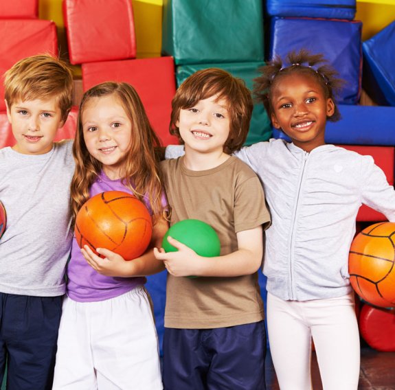 Lächelnde Kinder halten jeweils einen Ball und sich an den Schultern