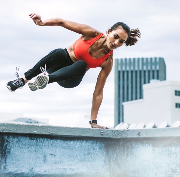 Eine Frau in Sportkleidung springt seitwärts über eine Mauer