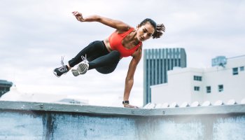 Eine Frau in Sportkleidung springt seitwärts über eine Mauer