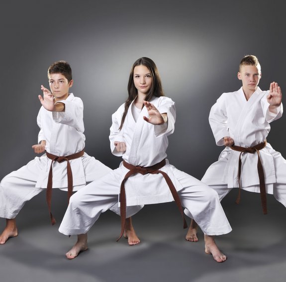 Ein Mädchen und zwei Jungs in Karateanzug vor grauem Hintergrund