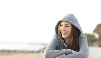Eine lachende Jugendliche mit grauem Hoodie sitzt am Strand