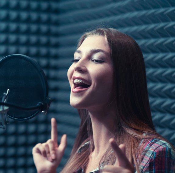 Eine junge Frau singt in einem Tonstudio in ein Mikrofon