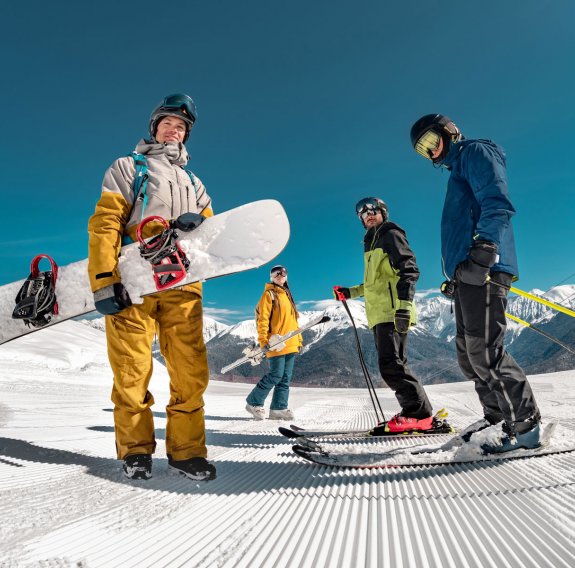 Drei Skifahrer und ein Snowboarder sind im Schnee zu sehen