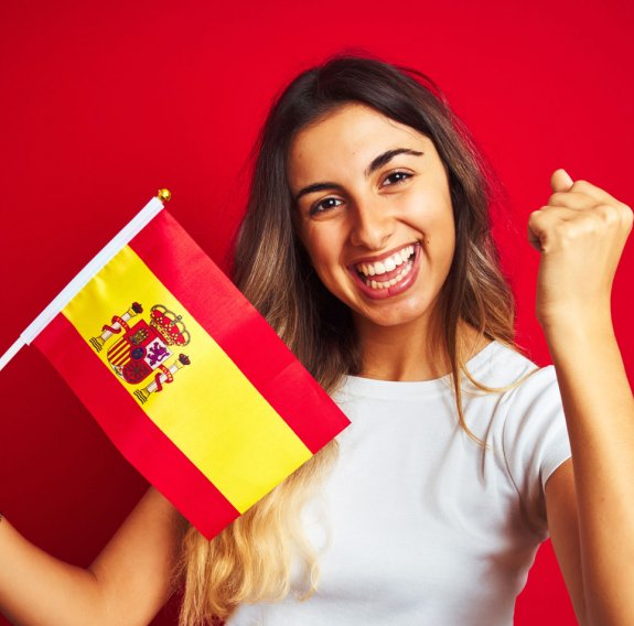 Eine lächelnde Frau hält eine spanische Flagge und gewinnend die Faust hoch