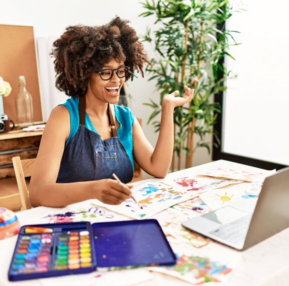 Eine fröhliche Frau malt vor einem Laptop 