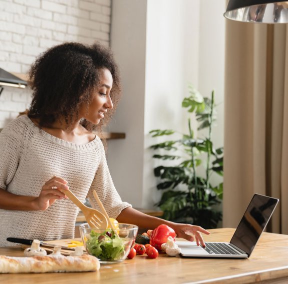 Eine Frau kocht vor einem Laptop