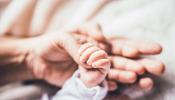 Mama die ihr frischgebackenes Baby an der Hand hält