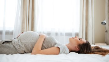 Schwangere Frau liegt glücklich nach dem Coaching im Bett